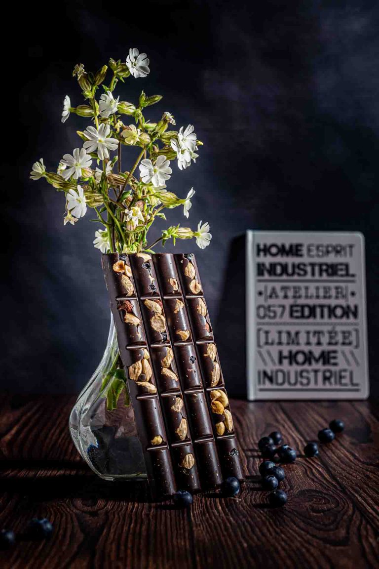 Photo d'aliment, une tablette de chocolat appuyé contre un vase avec des fleurs.